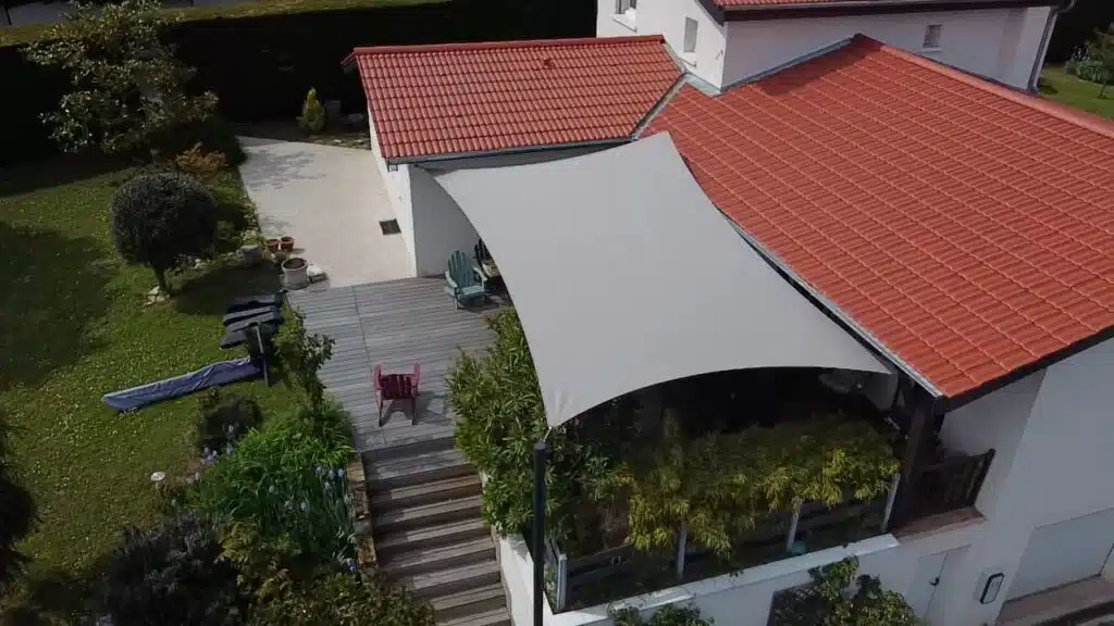 Voile d’ombrage double courbures taupe en toile Soltis 92 installée sur la terrasse d’une maison à Millery