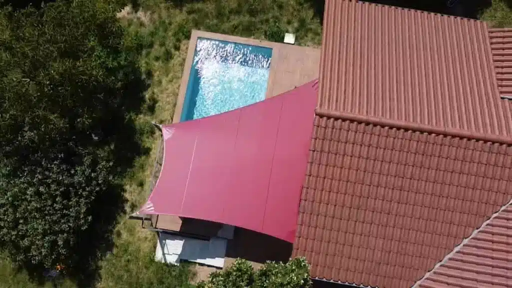 Voile vrillée rouge profond en toile Soltis 92 installée au-dessus d’une terrasse avec piscine à Vaugneray