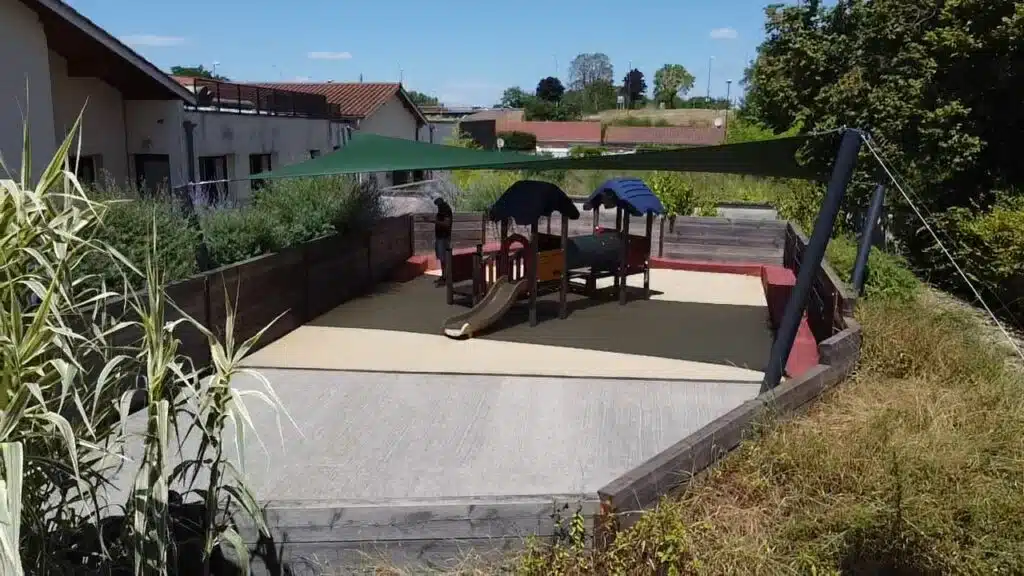 Installation d’une grande voile d’ombrage verte en toile Australe au-dessus d’une aire de jeux pour enfants à Ambérieu-en-Bugey.