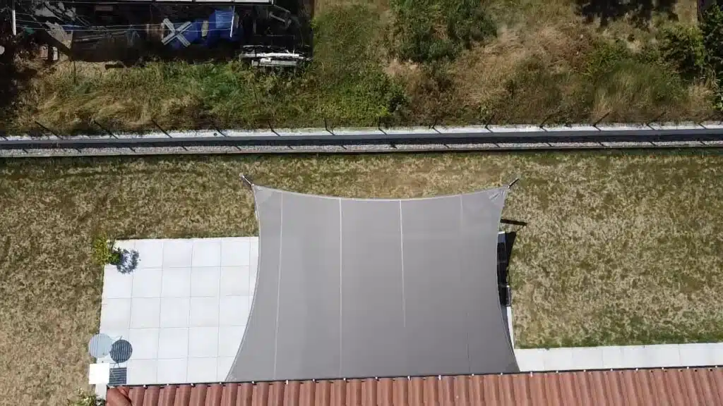 Vue du dessus montrant la forme vrillée de la voile d’ombrage bronze au-dessus de la terrasse.