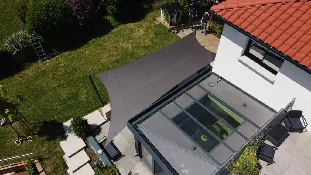 Voile d’ombrage Soltis 92 couleur bronze installée au-dessus d’une véranda et d’une terrasse à Brindas